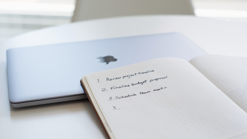 Il Reset Che Mi Ha Salvato la Settimana (e Probabilmente il Mese) Lista di 3 priorità scritta a mano su taccuino con laptop - metodo per ritrovare focus e produttività dopo gli imprevisti